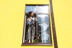 un mujer a mano lavados el ventana de el casa con un trapo con un rociar limpiador y un fregona afuera. la seguridad a altura, restaurar orden y limpieza en el primavera, limpieza Servicio foto