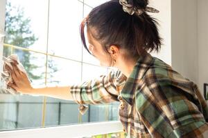 Woman manually washes the window of the house with a rag with spray cleaner and mop inside the interior with white curtains. Restoring order and cleanliness in the spring, cleaning servise photo