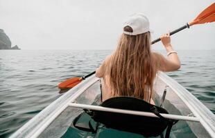 Woman in kayak back view. Happy young woman with long hair floating in transparent kayak on the crystal clear sea. Summer holiday vacation and cheerful female people relaxing having fun on the boat photo