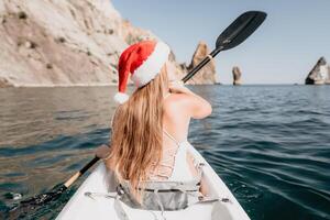 Woman in kayak back view. Happy young woman in Santa hat floating in kayak on calm sea. Summer holiday vacation and cheerful female people relaxing having fun on the boat. photo