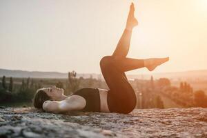 Fitness woman. Happy middle-aged fitness woman doing stretching and pilates on a rock near forest at sunset. Female fitness yoga routine. Healthy lifestyle with focus on well-being and relaxation. photo