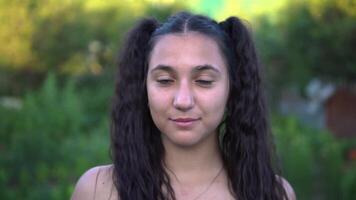 retrato. hermosa niña con largo pelo mira a el cámara y sonrisas en contra el antecedentes de naturaleza video