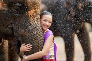 Beautiful rural Thai girl wear Thai northern traditional dress hug trunk of Asian elephant with blurred of water spray and any elephant background. photo