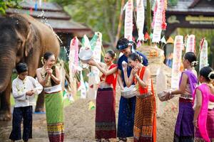 grupo de tailandés mujer y niños mercancía tailandés tradicional vestir jugar a salpicaduras agua en el tailandés nuevo años día o Songkran festival en un divertido camino en elefante y pila de arena antecedentes. foto