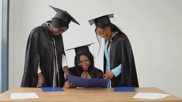 One woman is sitting at a desk, and two classmates are standing behind her, looking at graduation notes. video