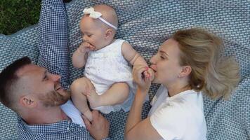 Father, mother and baby daughter lying on the mat in the middle of the lawn. Summer vacation outside the city or in the yard of a private house video