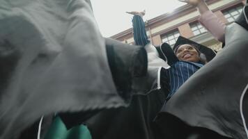 Happy graduates of university or college in master's robes and square hats hold hands together, demonstrating team spirit. Bottom view. African-American female students in Europe video