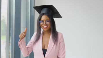 An African-American graduate woman in a light pink classic suit and a square master's hat poses and dances cheerfully and energetically. . Higher education for women abroad video