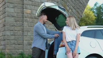 glücklich Paar Reisen durch Wagen. Mann und Frau falten Koffer zu das Kofferraum von ein Wagen. aktiv Freizeit zum jung Menschen video