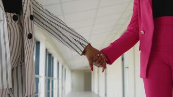 africain américain lesbienne couple. femelle mains. deux glamour africain femme d'affaires dans blanc rayé costume et rose costume tenir mains ensemble dans le salle de le Bureau centre video