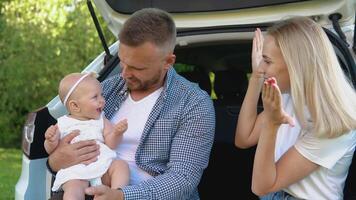 Family leisure outside the city. White family car. Happy father, mother and baby. Caring for babies. Father holds baby daughter in his hands video