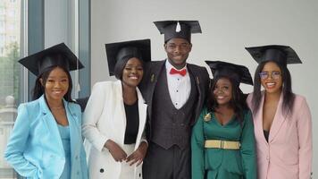 A young cheerful young man and four happy girls, university graduates stand in front of the camera in master's hats. Sincere smile video