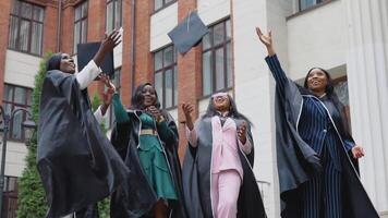 Happy graduates of a university or college of African American nationality in square robes throw up square hats of the master upwards. Student exchange program. Higher education for women in Europe video