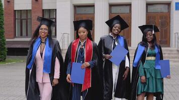 Happy graduates of a university or college of African American nationality with blue diplomas in their hands posing in front of the university video