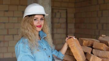 Beautiful woman with makeup and manicure holding a brick at the construction site. Woman in a helmet and working jeans video