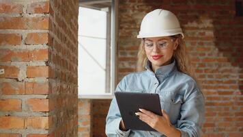 A female architect or bricklayer stands in a newly built house with untreated walls with a tablet in her hands. The process of building housing for the family. Building materials video