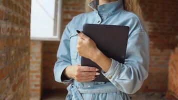 een vrouw architect of metselaar staat in een nieuw gebouwd huis met onbehandeld muren met een tablet in haar handen. modern technologieën in de oudste beroepen video