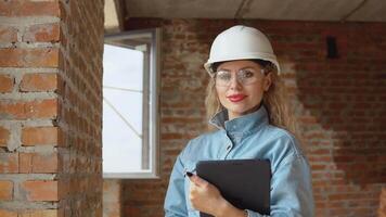 een vrouw architect of metselaar staat in een nieuw gebouwd huis met onbehandeld muren met een tablet in haar handen. modern technologieën in de oudste beroepen video