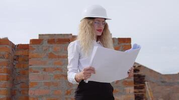 A female architect in business attire stands on the top floor in the open air at a construction site. The architect inspects the object according to the architectural plan video