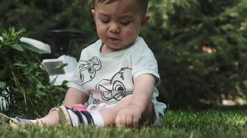 Taskent, Uzbekistán - 7 7 22 2023. un pequeño chico en un pantalones cortos se sienta en el césped en el parque y obras de teatro con un el plastico pelota. video