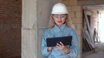 A female architect or mason stands in a newly built house with untreated walls and works on a tablet. Modern technologies in the oldest professions video