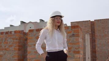 A female architect in business attire stands on the top floor in the open air at a construction site. The architect inspects the object video