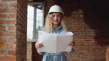 uma jovem mulher dentro uma branco trabalhos capacete e jeans roupas e óculos carrinhos às a construção local e detém uma construção plano. construtor, pedreiro, arquiteto video