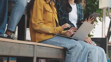 Group of happy young Asian college students sitting on a bench, looking at a laptop screen, discussing and brainstorming on their school project together. video