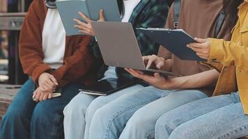 grupo do feliz jovem ásia Faculdade alunos sentado em uma banco, olhando às uma computador portátil tela, discutindo e debate em seus escola projeto junto. video