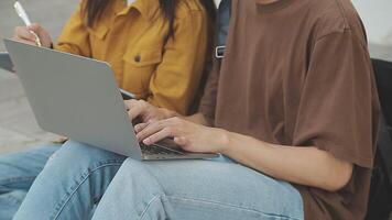 Group of happy young Asian college students sitting on a bench, looking at a laptop screen, discussing and brainstorming on their school project together. video