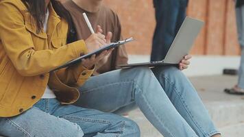 Group of happy young Asian college students sitting on a bench, looking at a laptop screen, discussing and brainstorming on their school project together. video