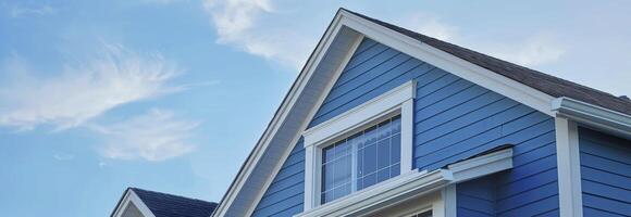 AI generated The top roof and gable on a blue house with white trim, against a blue sky background. photo