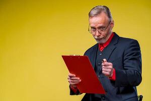 mayor empresario sentado con carpeta terminado amarillo antecedentes en traje mirando a cámara en rojo camisa . negocio concepto foto