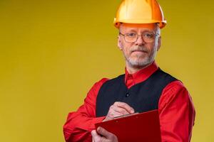 Middle aged businessman in helmet standing and holding file folder. Horizontal format isolated on yellow background. photo