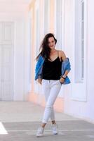 Summer in the city. Fashionable urban girl in casual clothes. Posing in big light hall. Long brown hair. Hands in pockets. photo