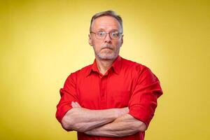 Confident middle aged man in red shirt with crossed hands over yellow background. photo
