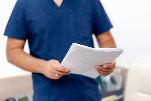 Portrait of doctor in scrubs. Medic holding printed diagnosis. Selective focus of hands with documents. Close up shot. photo