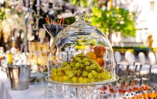 Grapes under glass transparent dome cover. Dessert on the festive table. Wedding table decoration. Selective focus. photo