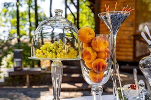 Dome crystal cover on plate with grapes. Peaches in vases. Blueberries in glasses. Luxury table decoration. photo