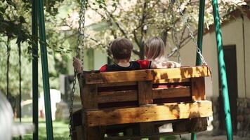 un adulte mère avec une Jeune fille balançant sur une balançoire dans le jardin suivant à sa maison. étreindre, parlant et en riant. video