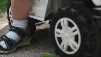 un joven madre en pantalones cortos paseos su pequeño hijo en un juguete coche. parque, soleado día. video