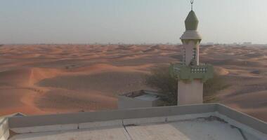 uma zangão moscas sobre uma pequeno Cidade com uma minarete coberto com deserto areia. video