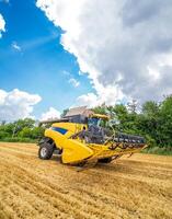 Yellow grain harvesting combine in a sunny day. Yellow field with grain. Agricultural technic works in field. Closeup. photo