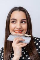 Palette with shades of teeth. Dental samples of tint teeth. Girl with red lips chooses perfect teeth color. Closeup. photo