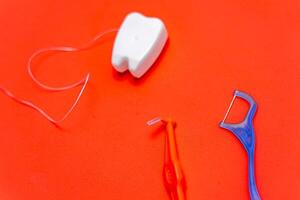 Different types of dental floss and tooth picks on red background. Dental floss in tooth toy shape. photo