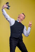 Senior man looking at camera while taking silly face selfie waving to the camera photo