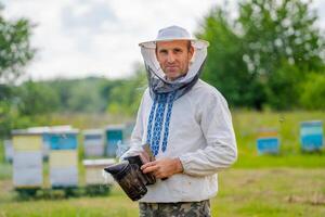 Beekeeper is working with bees and beehives on the apiary. Bee smoker in hands. photo