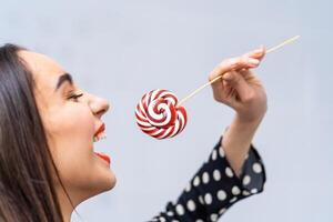 Pretty smiling brunette girl with a lollipop in her hand. Candy on stick. photo