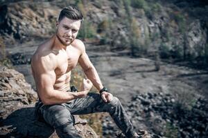 Man with perfect body pumping up muscles. Sitting on a quarry. Grey rocks background. photo