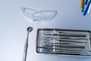 Metal dental instruments on table. Plastic protective glasses. Dental mirror near instruments. Oral care concept. photo